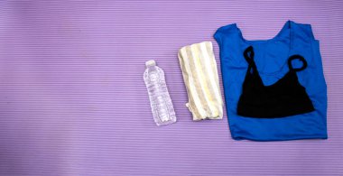 Healthy lifestyle, sport or athlete's equipment set : bottle of water with earphones and sneakers, towel and shirt, phone on purple mat with copy space