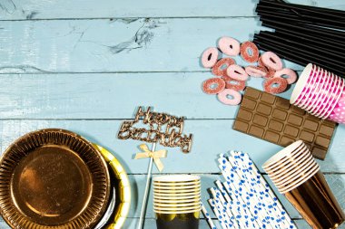 Doğum günü partisi: çikolatalı karton tabaklar ve jöleli şekerler, tek kullanımlık bardaklar ve pipetler ve tahta masada mutlu yıllar mesajı.