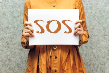 closeup woman holding paper with SOS text, refugee crisis concept