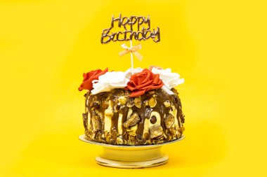 Birthday layer cake decorated with chocolate pieces and hazelnuts and almonds and hazelnuts and roses flowers and text