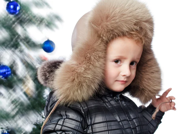 Menino com um chapéu quente no fundo da árvore de Natal — Fotografia de Stock