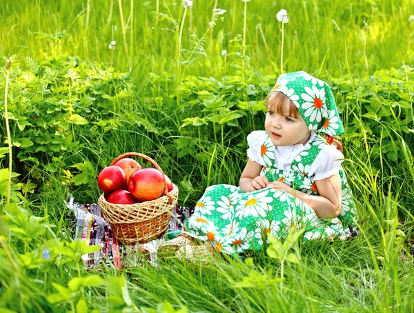 Baby girl is sitting on a glade and eating apples — Stock Photo, Image
