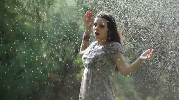 A beautiful girl begins to bustle on a lawn under a fountain — Stock Video