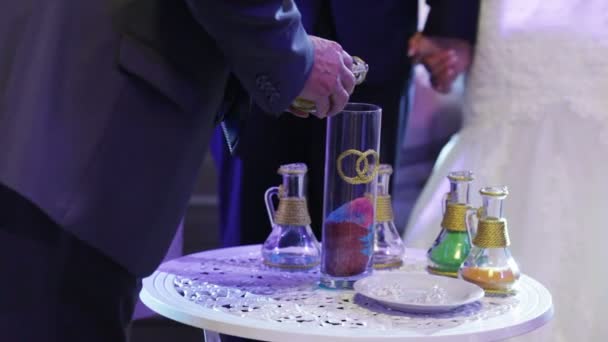 The bride's parents are mixed multicolored sand in the sign of the unity of families — Stock Video