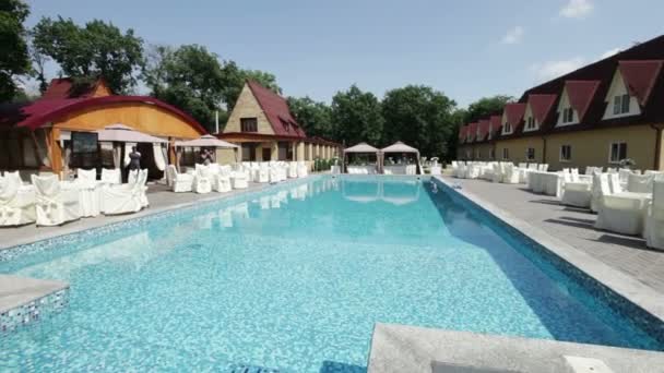 De camera vliegt rond het zwembad met tabellen omheen in een spa-hotel — Stockvideo
