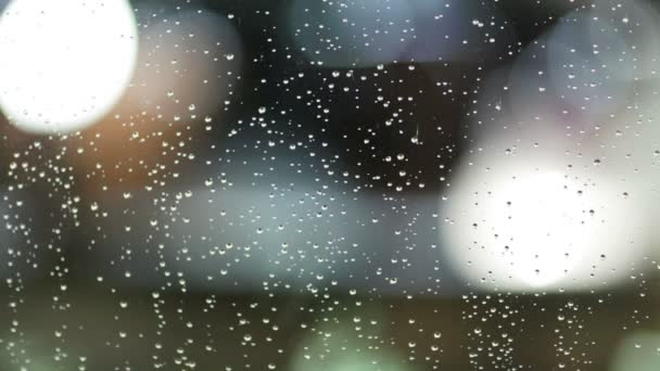 Вечерняя улица в Дефокус через стекло в капли дождя — стоковое видео
