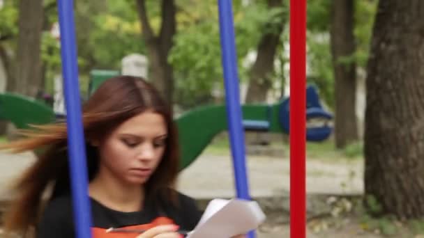 Chica en un columpio, escribiendo poesía en el parque de otoño — Vídeos de Stock