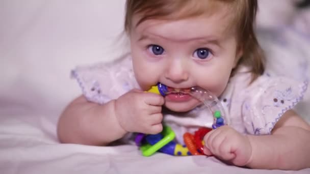 Bebê menina sorri e leva em sua boca chocalho brilhante — Vídeo de Stock