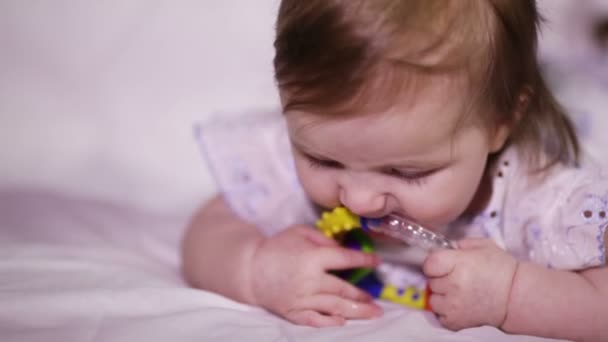 Bebê menina sorri e leva em sua boca chocalho brilhante — Vídeo de Stock