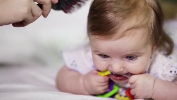 Mama dziecka czesanie, który się uśmiecha i ma w jej ustach jasne grzechotka — Wideo stockowe