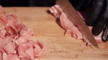 Ahşap bir tahtada jambon dilimleyen şef.