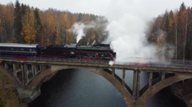 Karelia 'da bir nehrin üzerindeki köprüde bacadan duman çıkan buharlı lokomotif.
