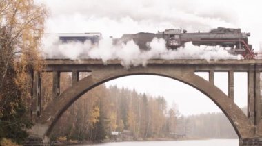 Karelia 'da bir nehrin üzerindeki köprüde bacadan duman çıkan buharlı lokomotif.