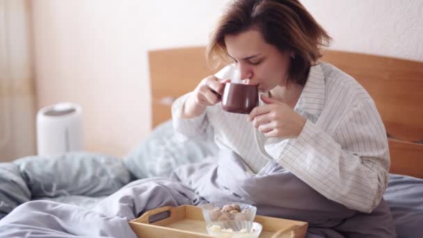 O fată frumoasă bea cafea și mănâncă popcorn în pat — Videoclip de stoc