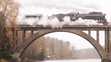 Karelia 'da bir nehrin üzerindeki köprüde bacadan duman çıkan buharlı lokomotif.
