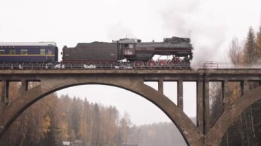 Karelia 'da bir nehrin üzerindeki köprüde bacadan duman çıkan buharlı lokomotif.