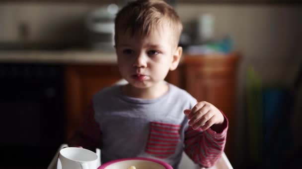 Трехлетний мальчик кашлял и ел печенье, сидя за стулом. — стоковое видео