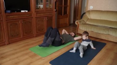 Oğlu ve babası minderde yoga yapıyor.
