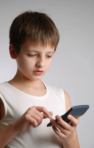 Menino pré-adolescente com telefone celular no fundo claro — Fotografia de Stock