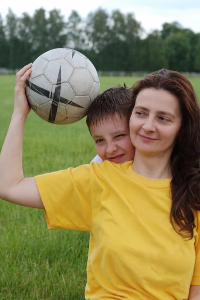 Woman holds football, boy peeps out from behind her — Stock Photo, Image