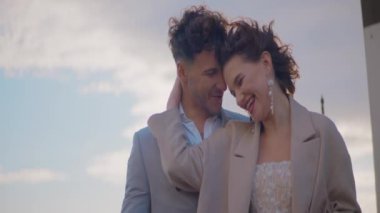 Yeni evliler bulutlu gökyüzünün arka planında sarılırlar. Başla. Güzel yeni evliler bulutlu havada mutlu bir şekilde sarılır. Yeni evliler şık kıyafetler içinde rüzgarlı havada sarılırlar.