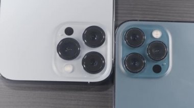 Saint Petersburg - Rusya, 10.11.2021: Yeni iPhone 13 'ün en fazla üç kamerasını kapatın. Başla. Şık tasarım ve ahşap yüzeyde duran yeni mavi ve gümüş akıllı telefonların profesyonel kameraları..