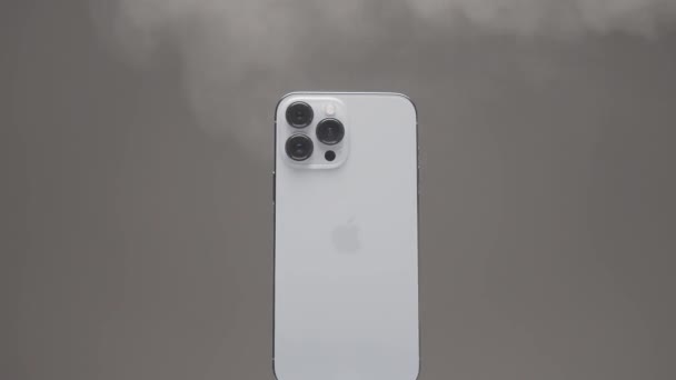 Нью-Йорк - США, 10.11.2021: закрытие нового iPhone 13 pro max с тремя камерами. Начали. Пар распространяется по новому серебряному смартфону, медленно вращающемуся на бежевом фоне. — стоковое видео
