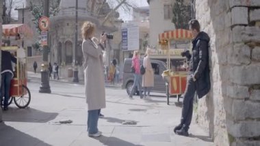 Eski Avrupa şehrinde genç bir adamın fotoğraflarını çeken bir kadın. Başla. Kameralı bir adamın fotoğrafını çeken kadının yan görüntüsü. Eski kasabadaki profesyonel kamerada adam vurmak.
