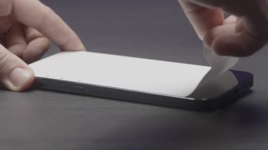 Servis merkezindeki akıllı telefondan ekran koruyucuyu kaldırmayı kapat. Başla. Erkek eller siyah akıllı telefon ekranından beyaz bir film çekiyor..