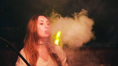 Dinlenme odasında su piposu içen bir kadının portresi. Medya. Uzun kızıl saçlı ve boynunda siyah boyunlu bir kadın Shisha barında dinleniyor..