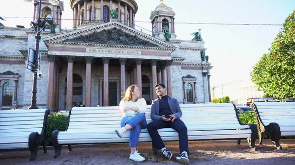 一对年轻夫妇坐在俄罗斯圣彼得堡圣以撒大教堂附近的长椅上。媒体。男人和女人坐在一起，像朋友一样聊天. — 图库照片