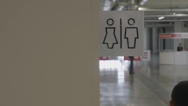 Крупним планом логотип чоловічої та жіночої вбиральні на бежевій стіні всередині бізнес-центру. HDR. Вид ззаду чоловіка в білій сорочці, що проходить біля громадського туалету . — стокове відео