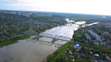 Helikopterden görüntü. Şarjör. Arabaları, gökyüzü, evleri ve yeşil yolları olan, nehri geçen küçük bir kasaba manzarası.