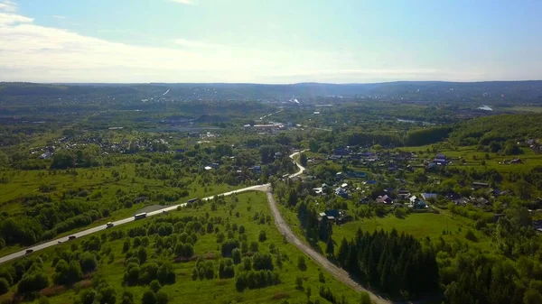 Blick von einer Drohne auf die Stadt. Clip. Eine sommerliche Provinzstadt mit einer kleinen Straße mit Autos, niedrigen Häusern, grünen, sonnigen Bäumen ringsum und einem strahlend blauen, sonnigen Himmel. — Stockfoto