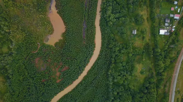 Un enorme río sucio en el bosque. La vista desde el dron. Clip. Un enorme río sucio curvado con productos petrolíferos que fluye junto a un enorme bosque verde y varias pequeñas casas para la gente son — Foto de Stock