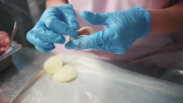 Παραγωγή στο κατάστημα τροφίμων. Κλιπ. Μια γυναίκα με ειδική ποδιά και γάντια φτιάχνει ζυμαρικά σε ειδικό σιδερένιο τραπέζι.. — Αρχείο Βίντεο