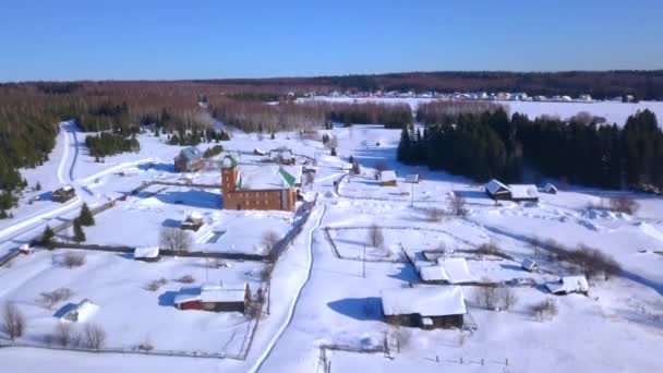Vinterutsikt från en drönare. Klipp. Byn ligger intill ett litet område med små hus bakom som är en bar kall vinterskog och en klarblå himmel. — Stockvideo