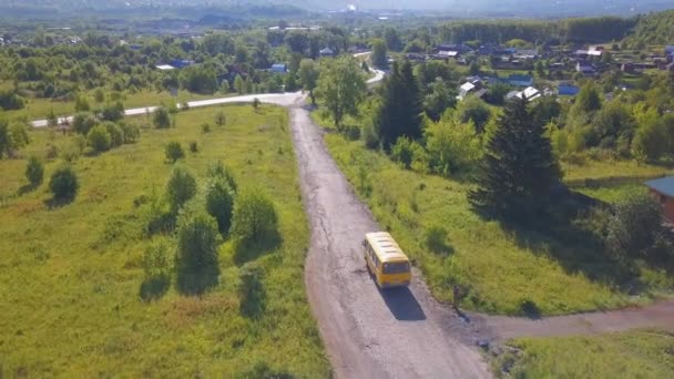 Vista de pájaro. Clip. Un largo camino en el que un autobús amarillo cabalga sobre un fondo de árboles verdes y hierba — Vídeos de Stock