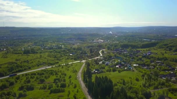 Blick von einer Drohne auf die Stadt. Clip. Eine sommerliche Provinzstadt mit einer kleinen Straße mit Autos, niedrigen Häusern, grünen, sonnigen Bäumen ringsum und einem strahlend blauen, sonnigen Himmel. — Stockvideo