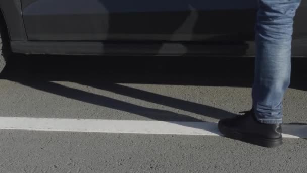男は運転手の側で車に乗り込む。HDR。アスファルト道路や乗用車の背景に黒い靴やジーンズで男性の足のクローズアップ. — ストック動画