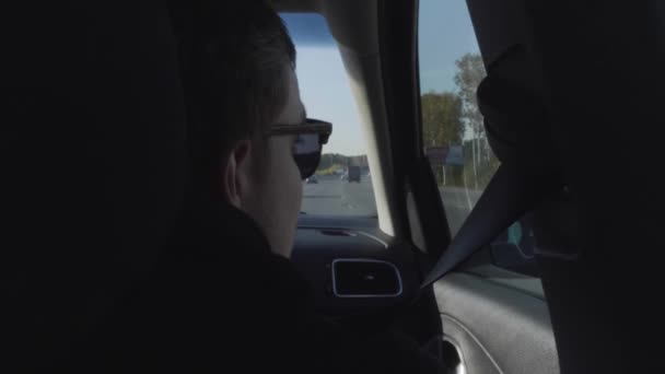 Widok z tyłu młodego człowieka w czarnych okularach przeciwsłonecznych spoglądającego przez boczne okno samochodu. Odbiór. Mężczyzna cieszący się letnią przejażdżką wewnątrz pojazdu. — Wideo stockowe
