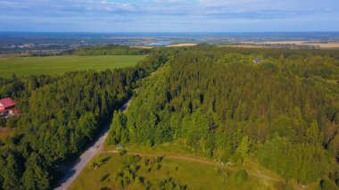 Drone 'dan tarlanın güzel manzarası. Şarjör. Kocaman yeşil bir Rus ormanı, bir yolu, ötesinde bir tarlası, açık mavi bir gökyüzü, bir nehir ve şehrin küçük bir parçası..