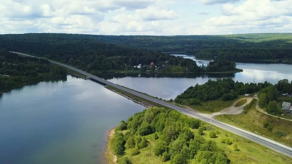 Un enorme puente sobre el río. Clip. Vista de pájaro. Un enorme puente sobre un gran río sobre el fondo de un cielo despejado y enormes árboles forestales. —  Fotos de Stock