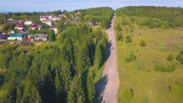 Vista de verano desde un dron en un pequeño pueblo. Clip. Un camino de verano con campos y bosques con pequeños edificios residenciales. — Vídeos de Stock