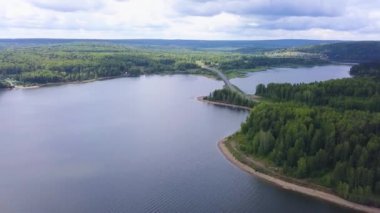 Nehir boyunca kocaman bir köprü. Şarjör. Kuş bakışı görüş. Büyük bir nehrin üzerinde bulutsuz bir gökyüzü ve büyük orman ağaçlarının arka planına karşı kocaman bir köprü..
