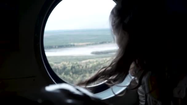 Uçak penceresinden bak. Şarjör. Dalgalı saçlı bir kız havalanan bir uçağın yüksekliğinden yeryüzünün manzarasına bakıyor. — Stok video