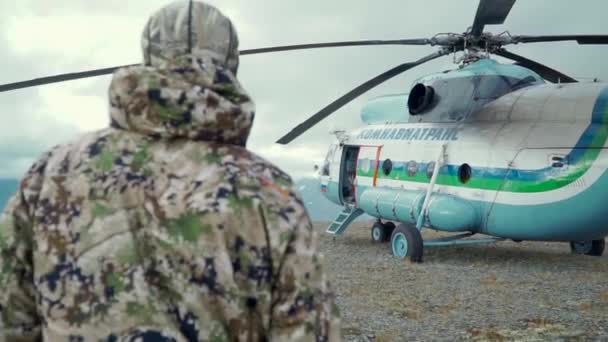Посадка на вертолет. Клип. Мужчины входят в вертолет, который стоит в лесу на фоне туманного неба и огромных гор. — стоковое видео