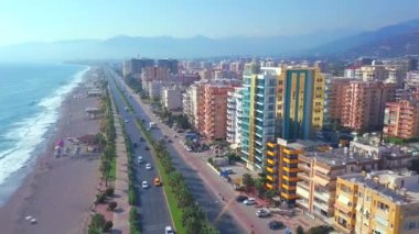 Denizin ve şehrin üzerinde uçuyor. Şarjör. Şehrin, yolun, arabaların ve plajın kuş bakışı görüntüsü.
