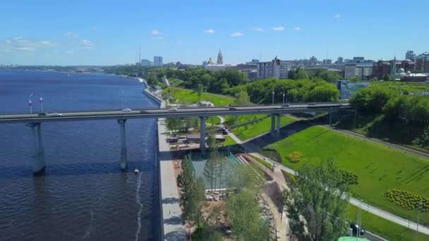 Η θέα από το τηλεκατευθυνόμενο. Κλιπ. Μια τεράστια γέφυρα που διασχίζει το ποτάμι με αυτοκίνητα δίπλα στο πάρκο και μεγάλα σπίτια. — Αρχείο Βίντεο