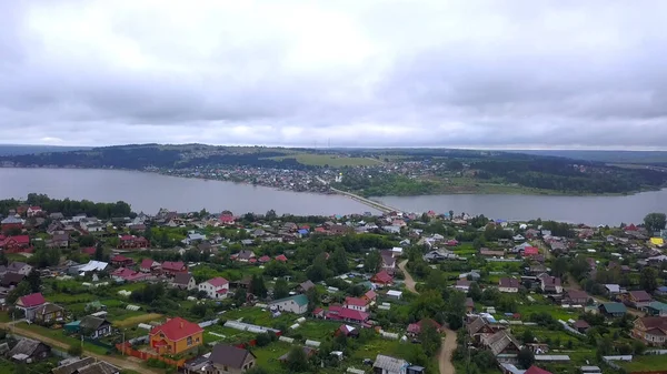 Sommerblick aus einer Drohne. Clip. Blick auf eine kleine Stadt mit einem Fluss, einer Brücke über einen Teich mit Autos, nahe gelegenen Parks, Wäldern und Häusern und einem leicht bewölkten Himmel. — Stockfoto